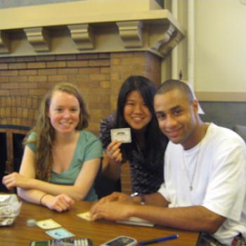Three students at a table with calculators. One holds up a card.