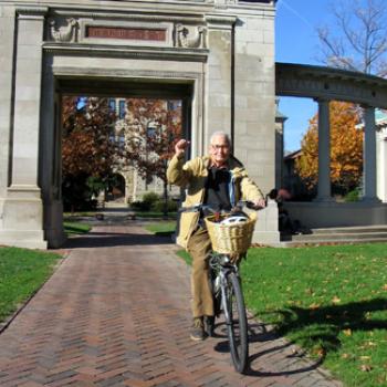 An older man with a raised fist rides a bike through Memorial Arch