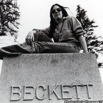 A young woman is seated atop a stone monument engraved with 'Beckett'