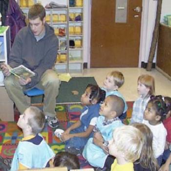 A college student reads to agroup of attentive preschoolers