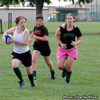 Rugby players run downfield. The one with the ball appears fearless.