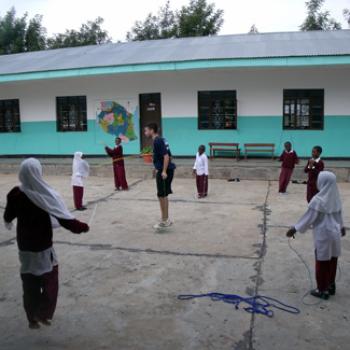 In a school courtyard, Mike teaches jump rope to a group of boys and girls.