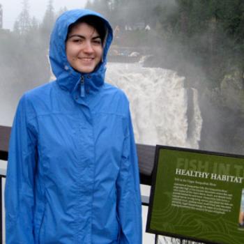 With a waterfall in the background, Miranda stands by an informational sign headlined Healthy Habitat.