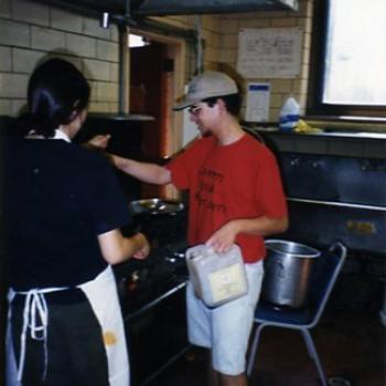 Two students cook food on a large stove.