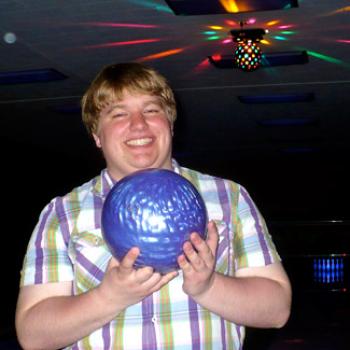 Patrick holds up a bowling ball under colorful lights.