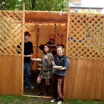 People with plates of food in a small wooden structure.