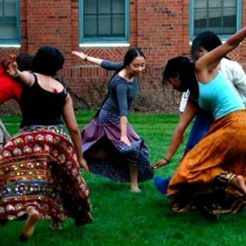 Women in colorful skirts dance in the quad.