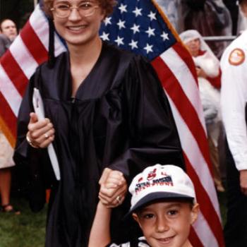 Sue holds her diploma in one hand and her son's hand in the other.