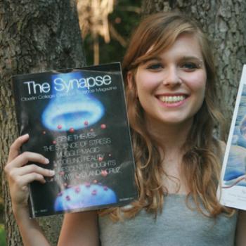 A woman shows the front cover of The Synapse magazine.