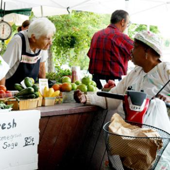 A woman asks a question at a fruits & vegetables stand.