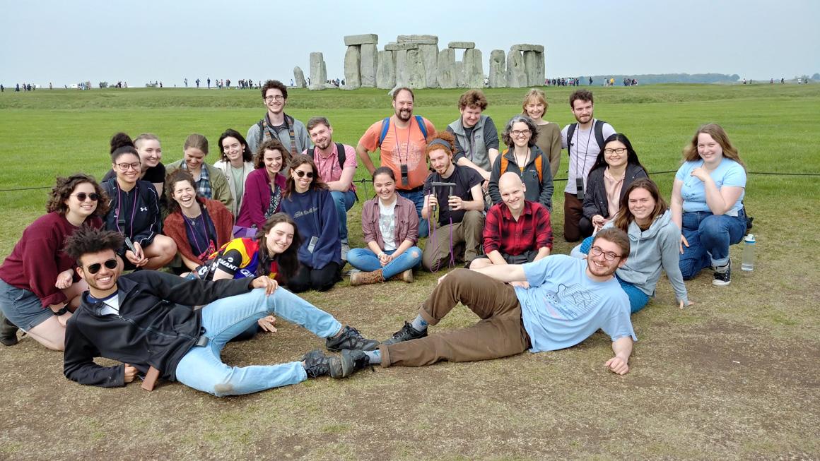 About 2 dozen people pose with the Stonehenge site in the background.