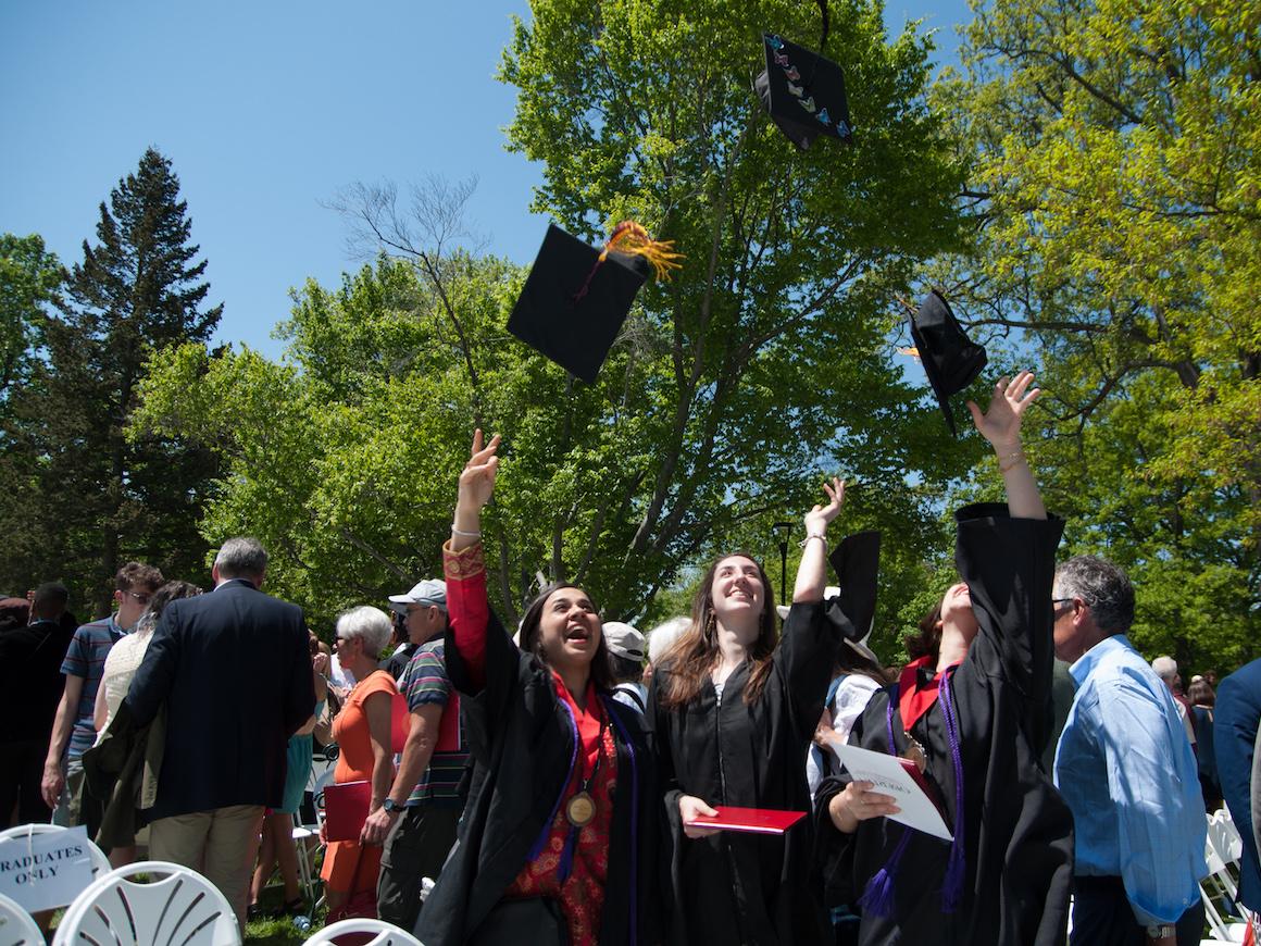 Graduates toss mortarboards into the air.