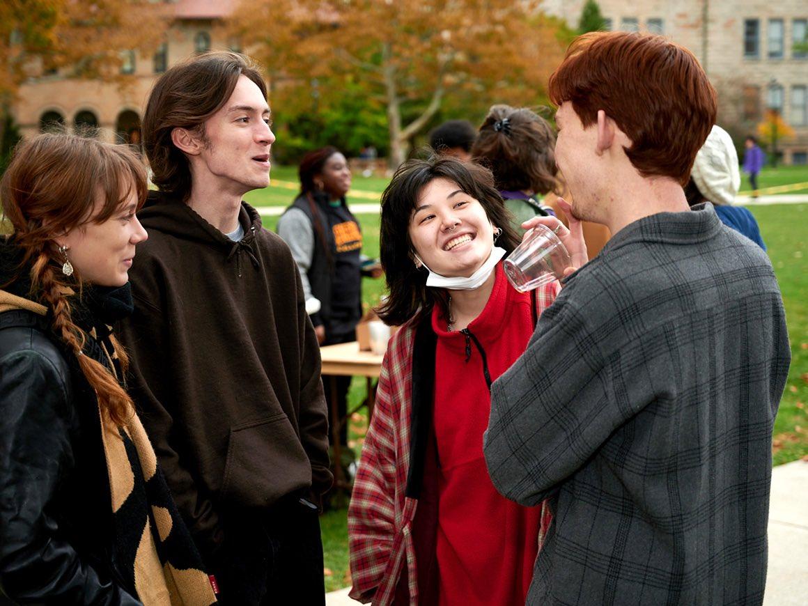 Four people share a laugh on a brisk fall day on campus.