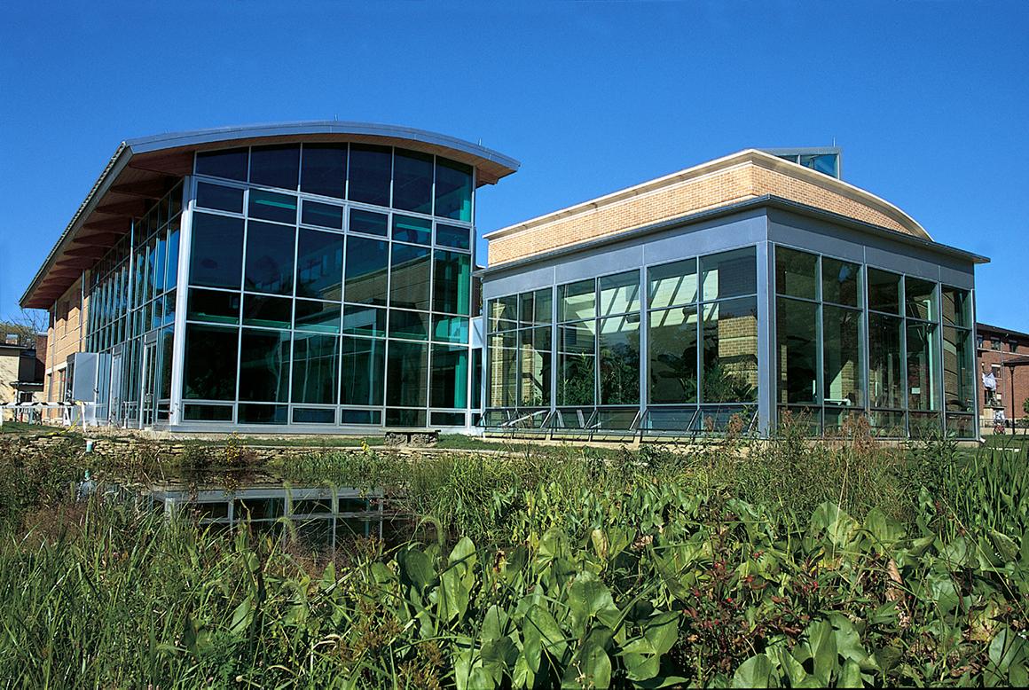 Exterior of a two-story, glass-walled building surrounded by vegetation