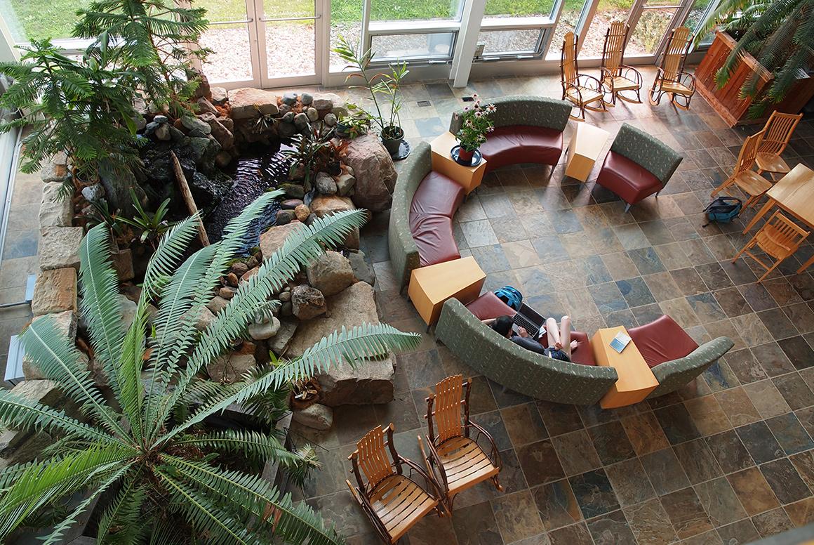 An atrium, viewed from above, features large plants, a rock garden fountain, and modern furniture arranged in a circle.
