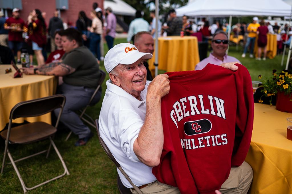 An elderly man holding up a vintage Oberlin Athletics sweater.