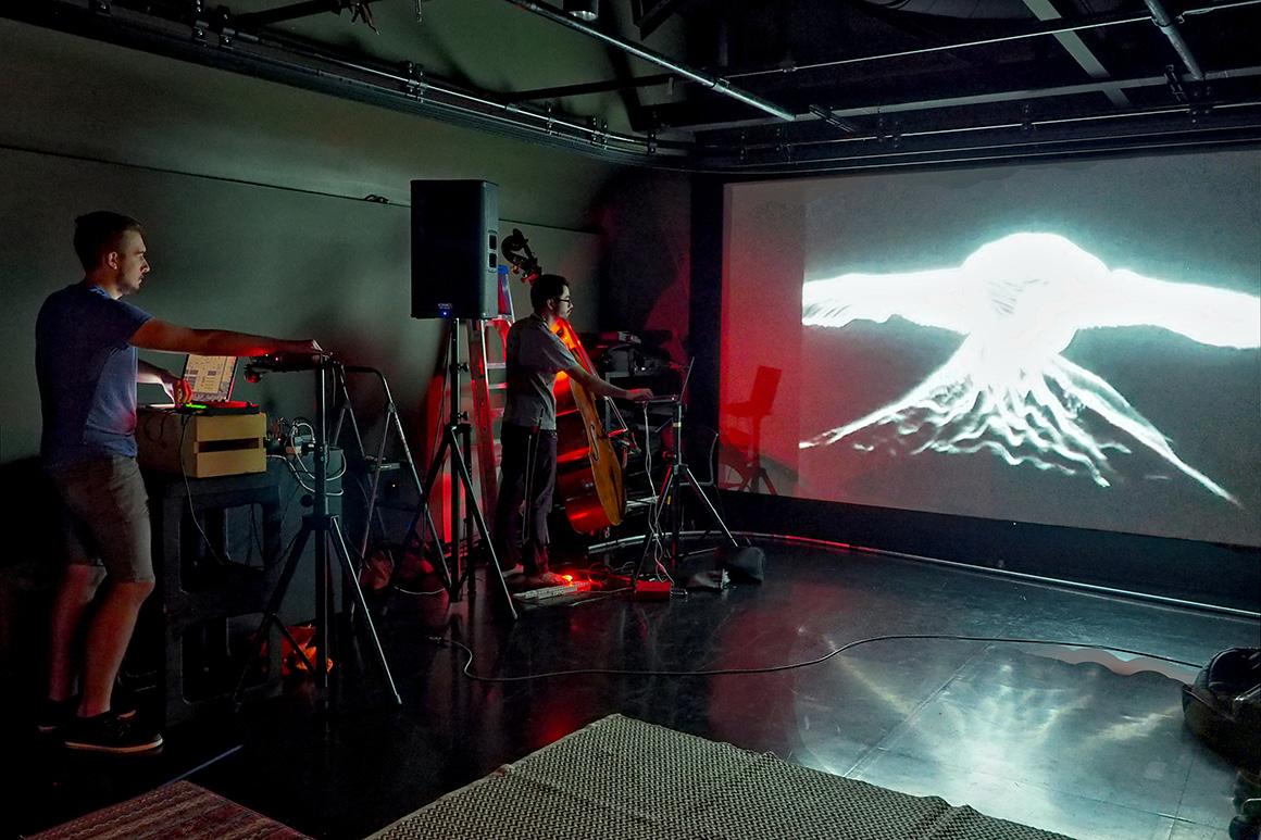 A multimedia performance includes a glowing projection behind a bassist.
