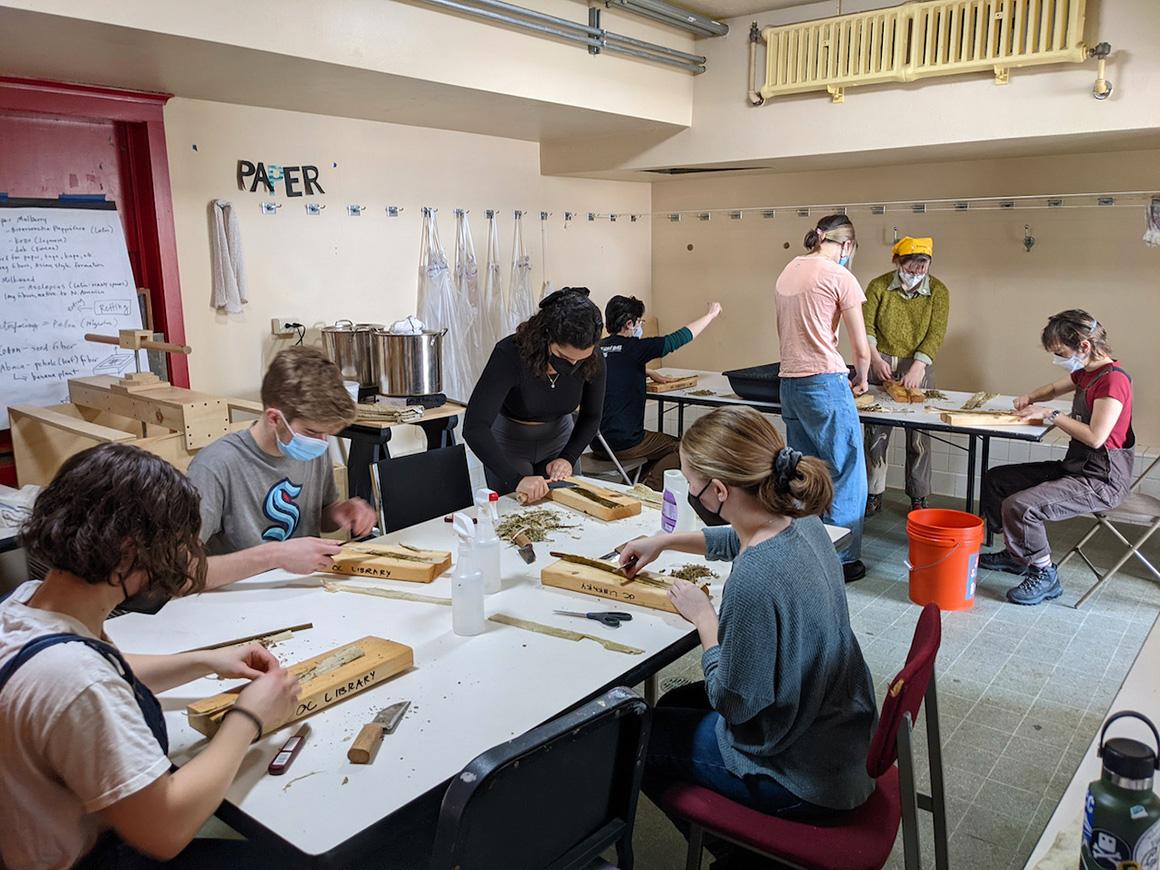 Students work with cutting tools seated around tables.