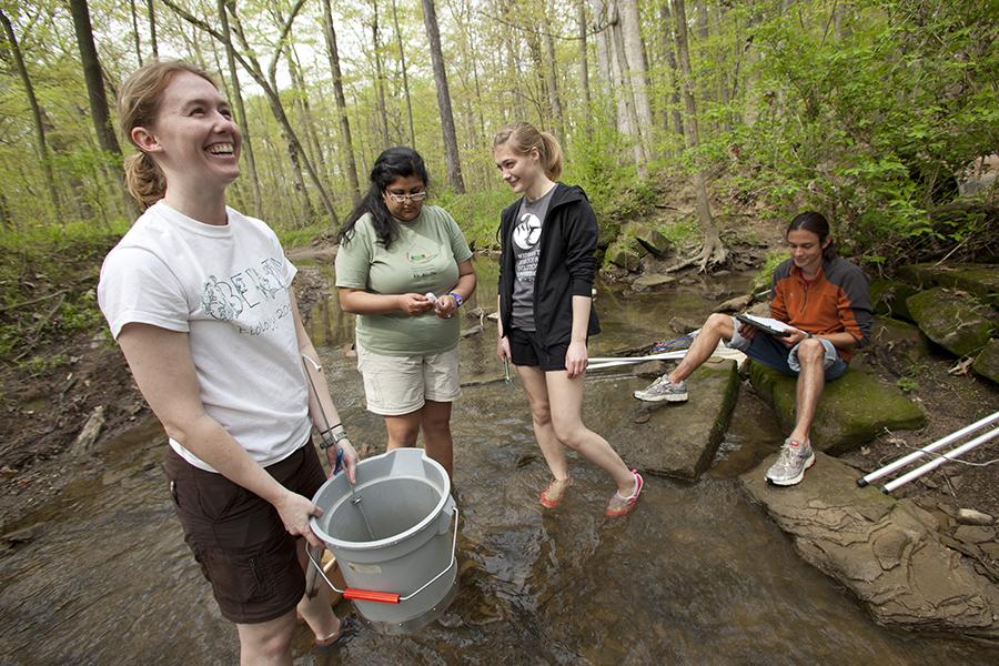 Students stand in a creek with buckets and gloves, smiling