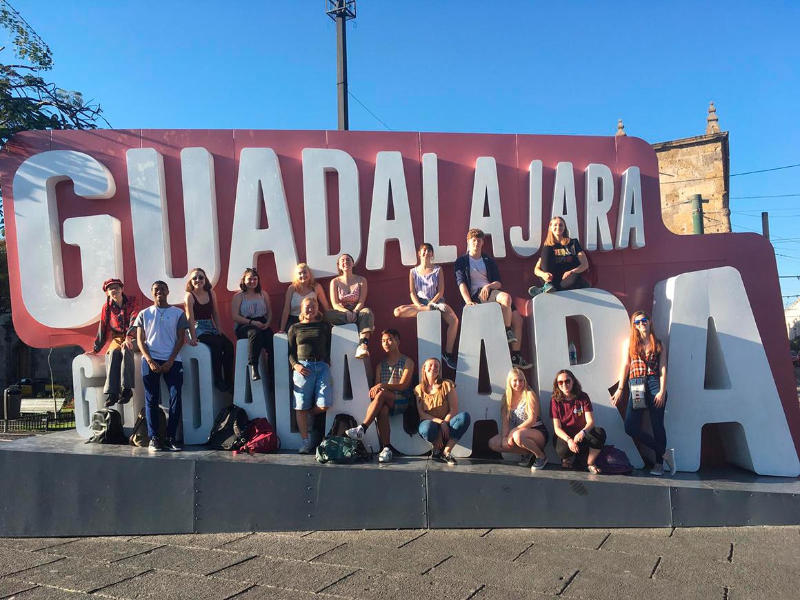 A group poses in front of, and on top of, a gigantic sign that reads Guadalahara.