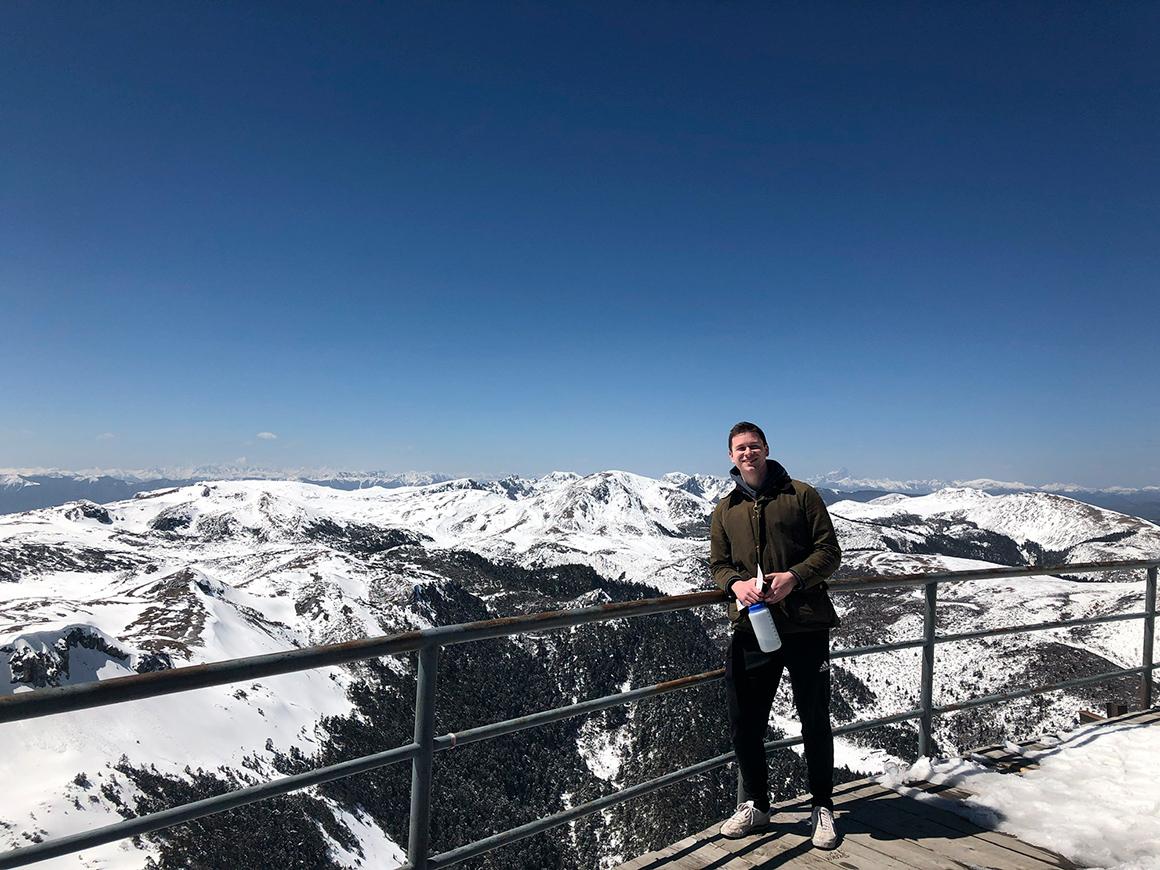 A student poses in front of snowy mountains.