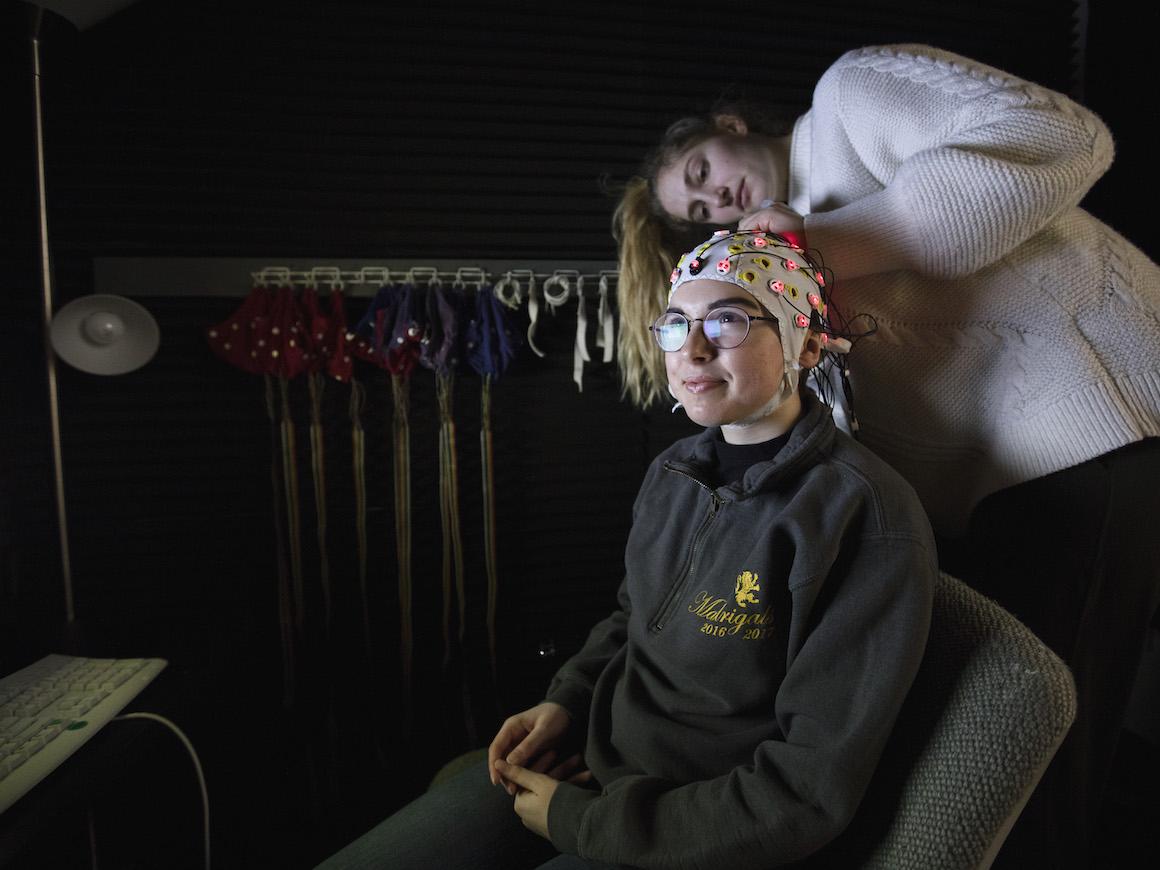 a student adjusts an EEG cap on another student.