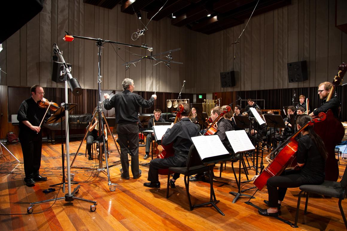 A string and wind ensemble in the recording studio with microphones all around.