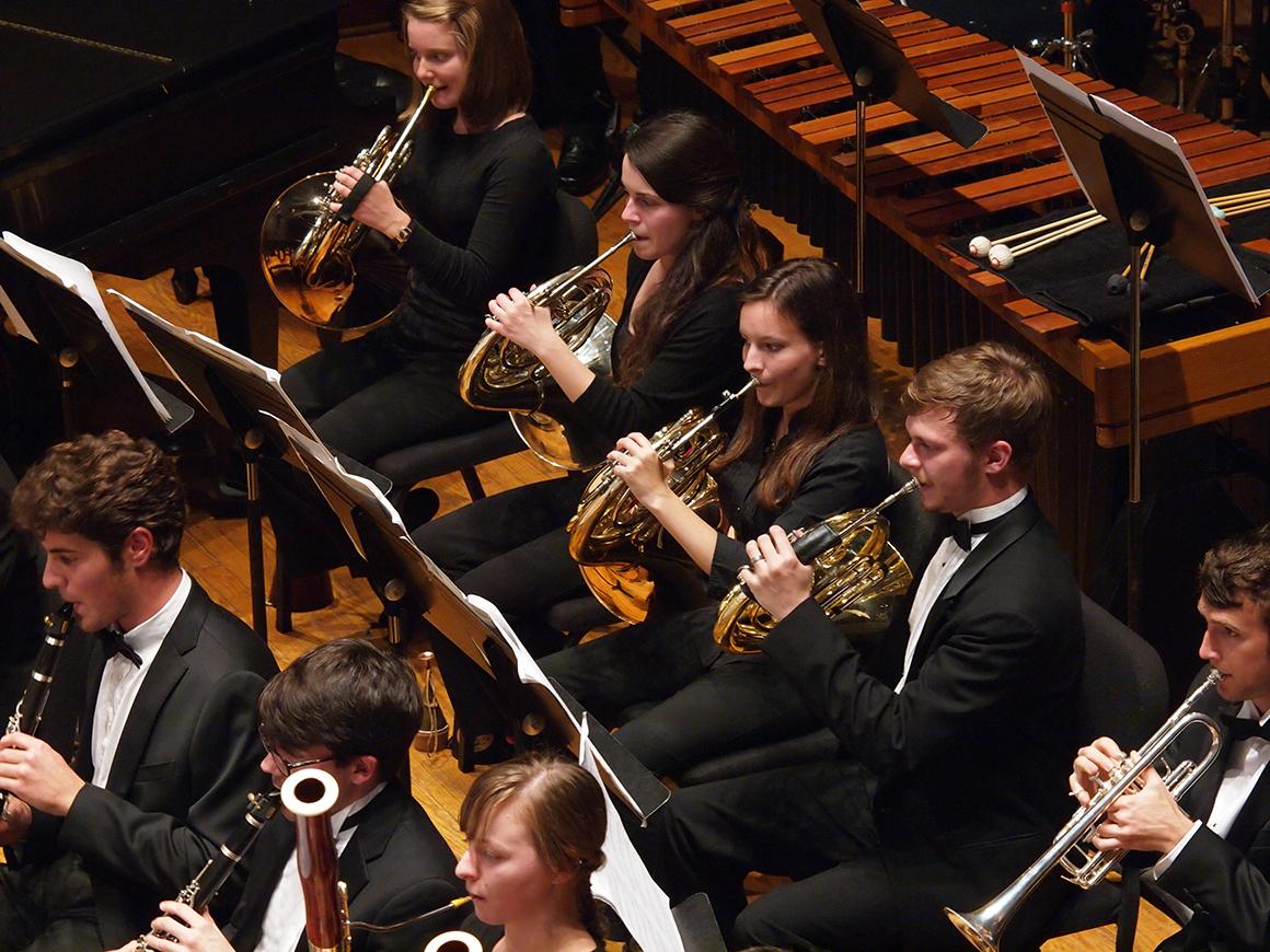Close-up of 4 French horn players performing in an orchestra.