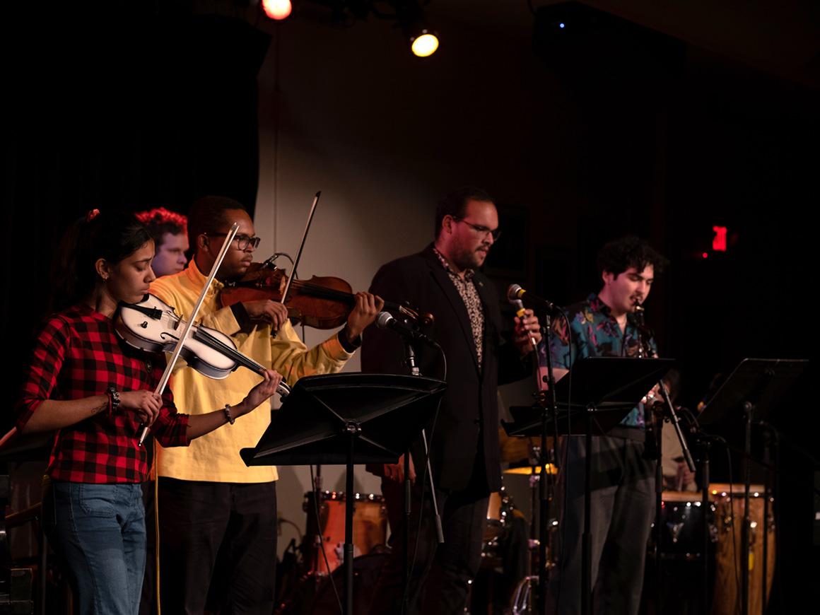 A small group of student musicians perform onstage in a club-like atmosphere.