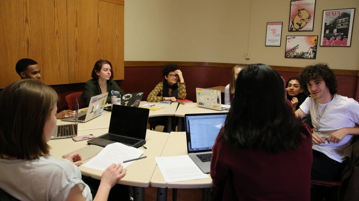 A group meets around a round table, laptops open and papers out.