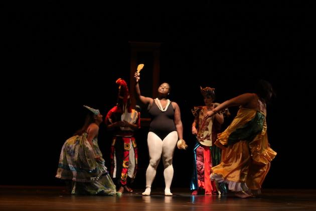 Students performing on stage. The student in the center has a black leotard and white tights on.