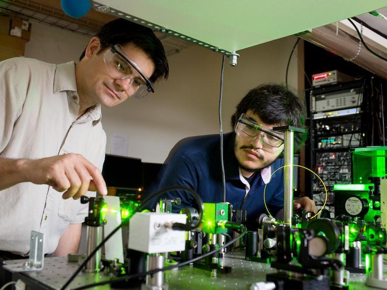 A professor and student work with glowing lab equipment.