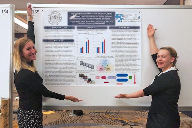 Two students show their research poster, which includes bar charts, a Venn diagram, and sections of text titled Introduction, Method, Results, and Summary.