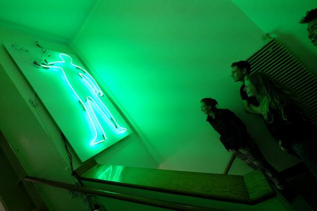 Students looking up at a green neon sign shaped like a human.