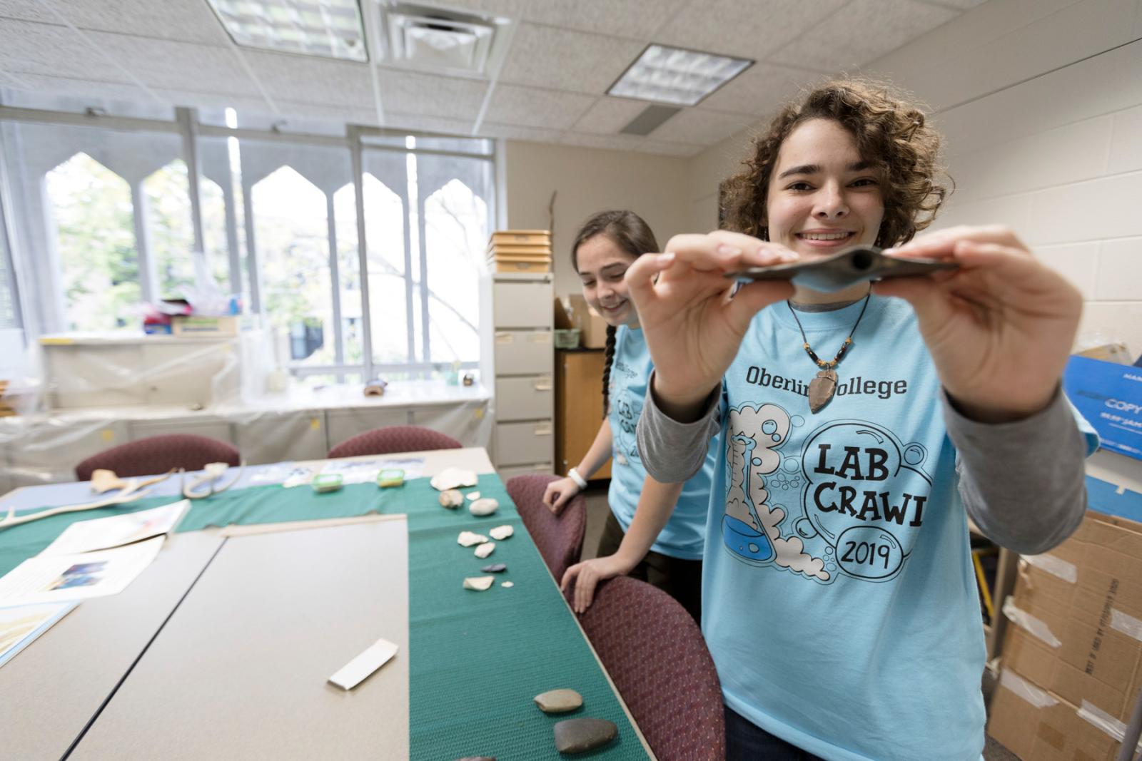 A student holds up an artifact. Her tee-shirt says Oberlin College Lab Crawl 2019.