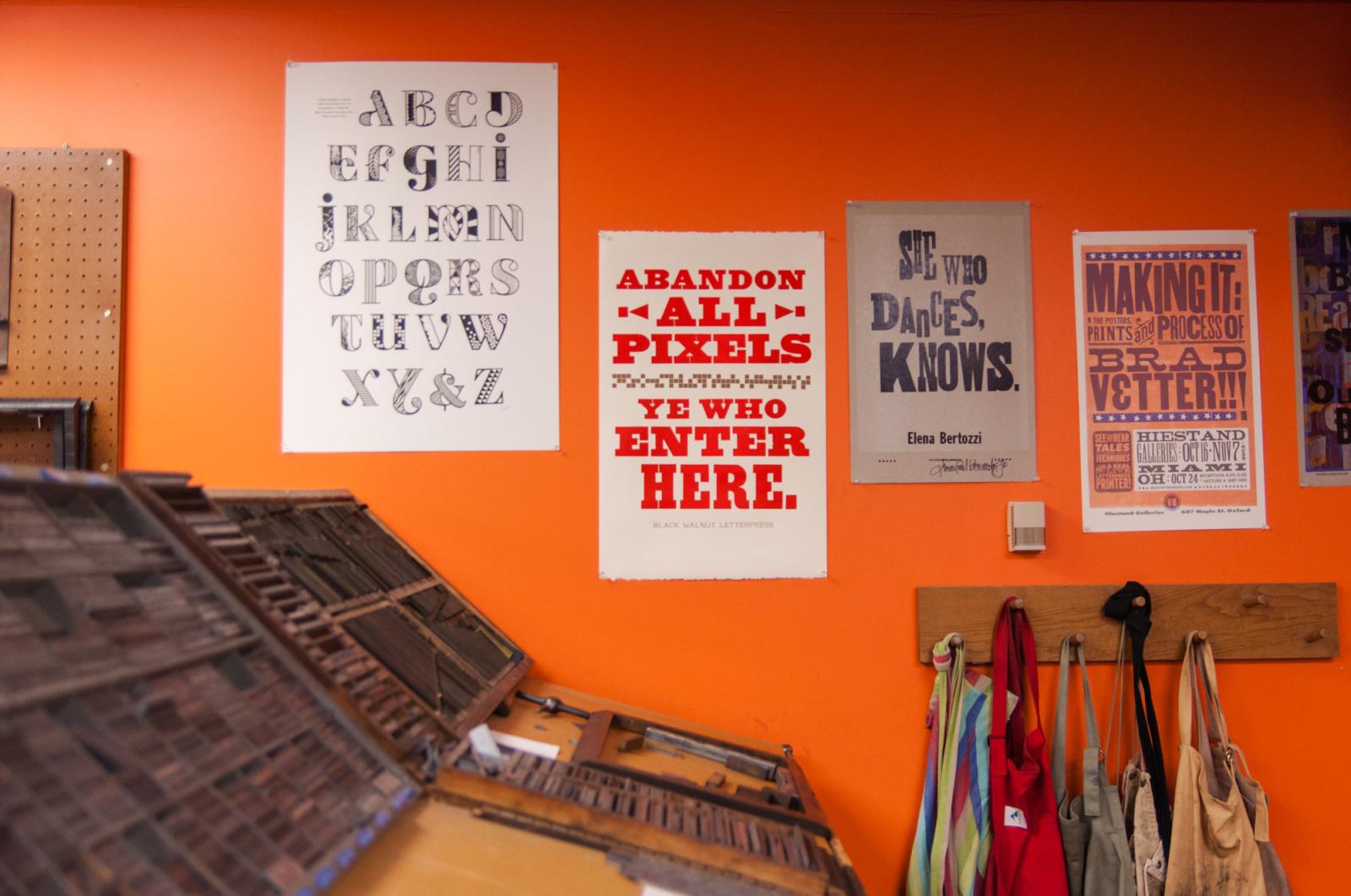 The wall next to some printing equipment features posters with a variety of bold and dramatic font faces.
