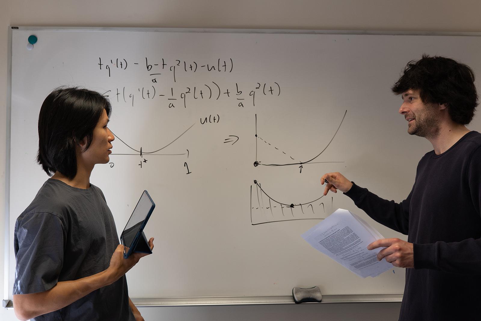 Professor and student talk while pointing at writing on a white board