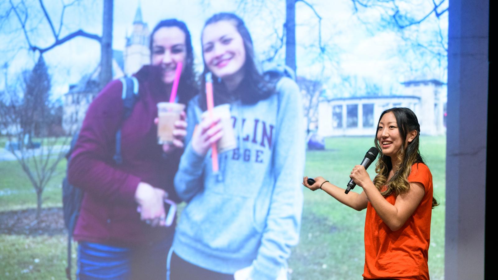 A student gives a slide presentation, which shows 2 students outdoors holding to-go drink cups with large straws. 