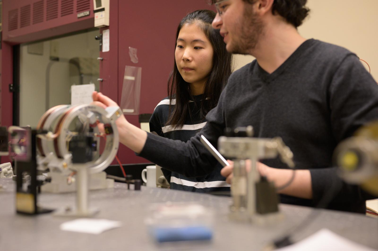 Two students at a lab bench make adjustments to a coil.