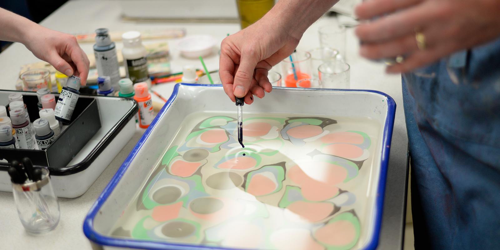 Students work with paints in a shallow pan, creating patterns.