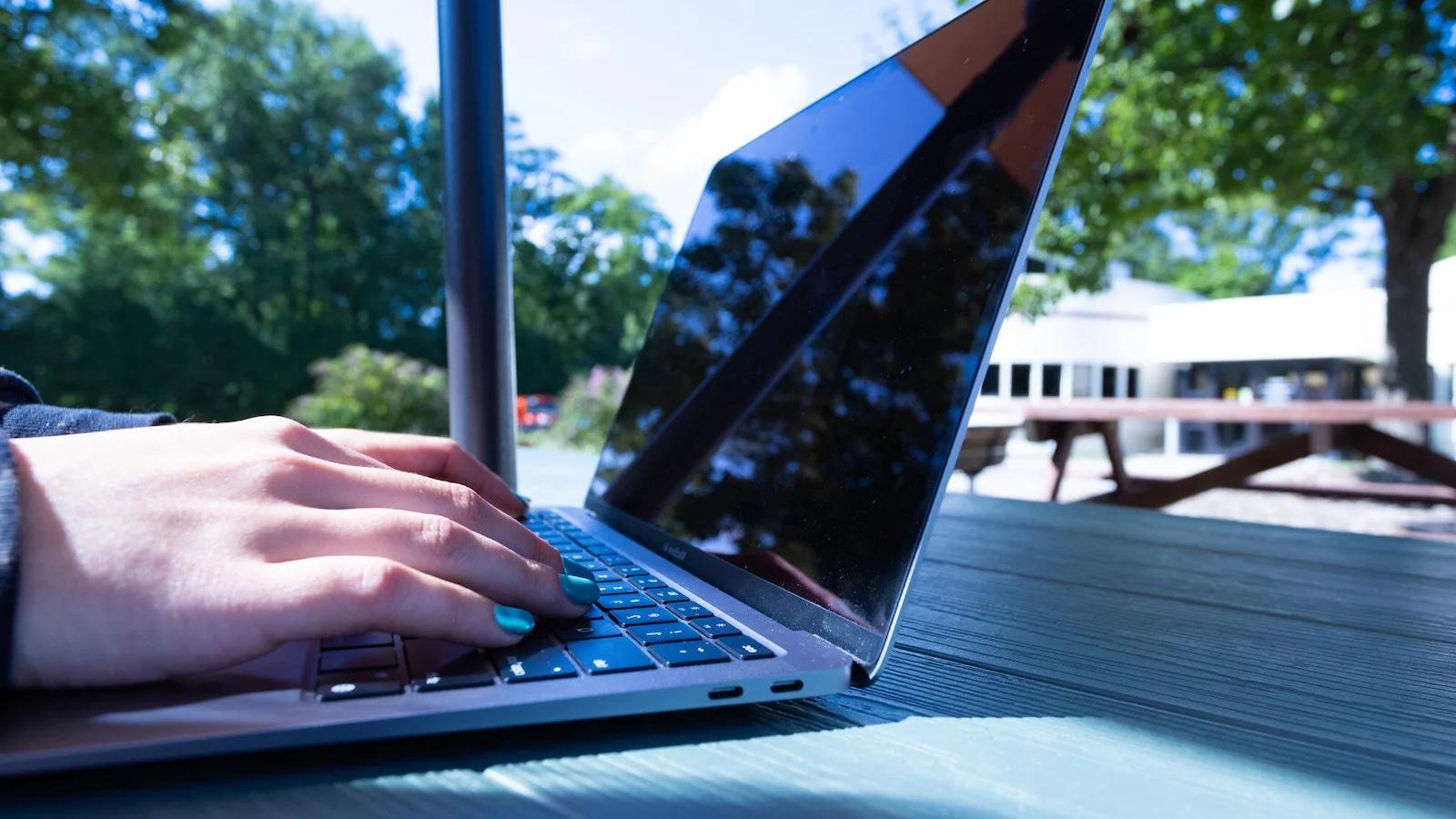 A student working on their laptop at a picnic table.
