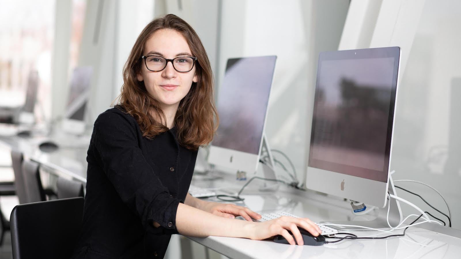A student wearing glasses sitting in front of a desktop computer.