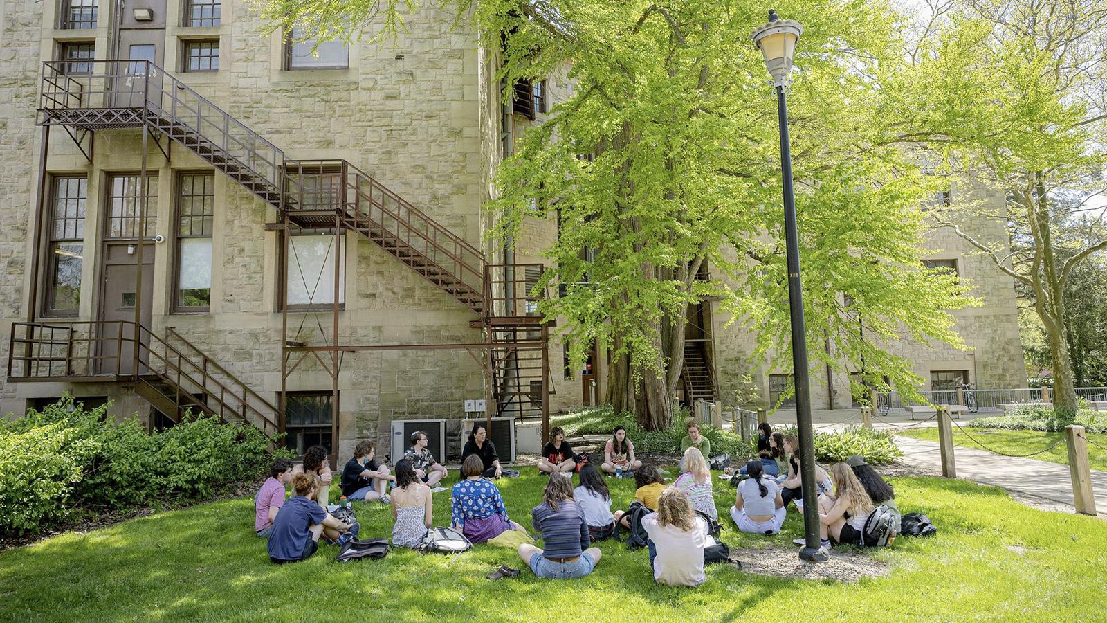 Jewish studies students sit in a circle in the grass behind a campus building