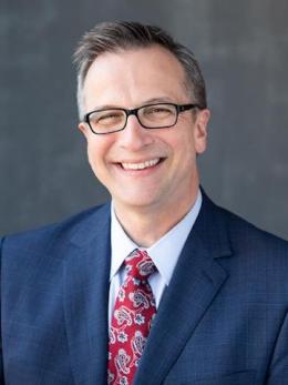 man in navy suit red speckled tie and glasses named Michael Grzesiak.