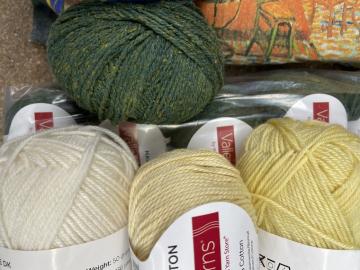 Several skeins of white and yellow yarn next to the green