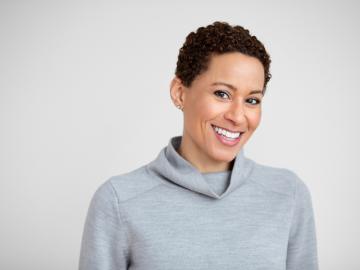 smiling woman with short curly brown hair wearing light blue-gray sweater