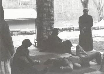 Three students lay on a concrete porch with two other students standing nearby.