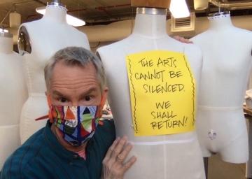A man wearing a mask holds a mannequin wearing a sign. 