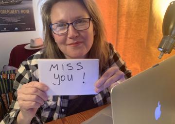 A woman holds a miss you sign.