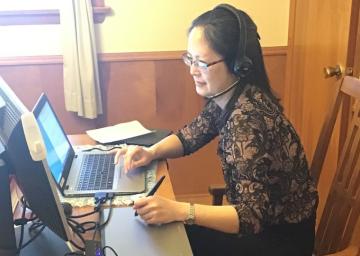 A woman wearing a headset, works on a laptop.